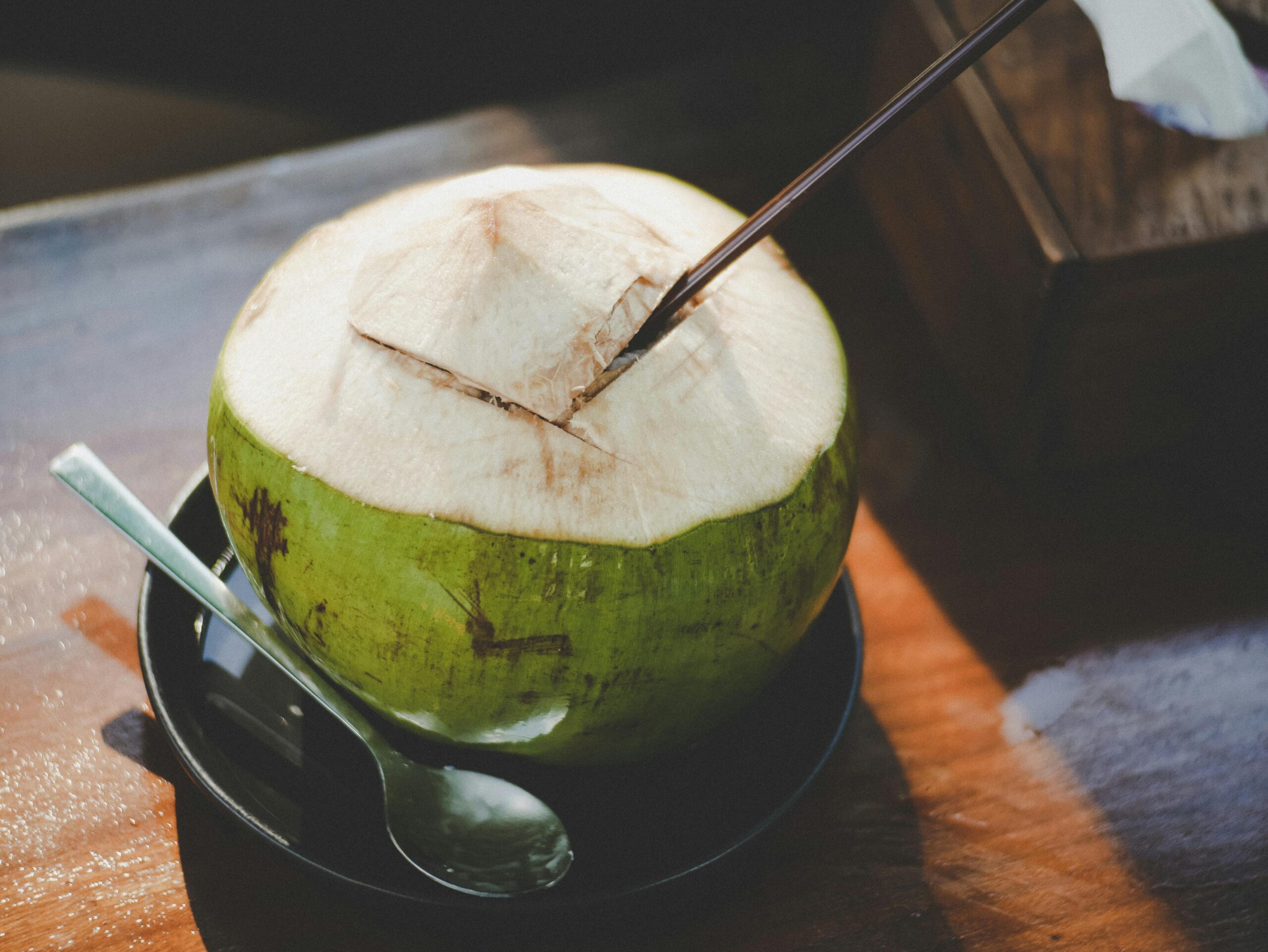 A close-up of a fresh coconut with a straw and spoon, beautifully captured indoors.
